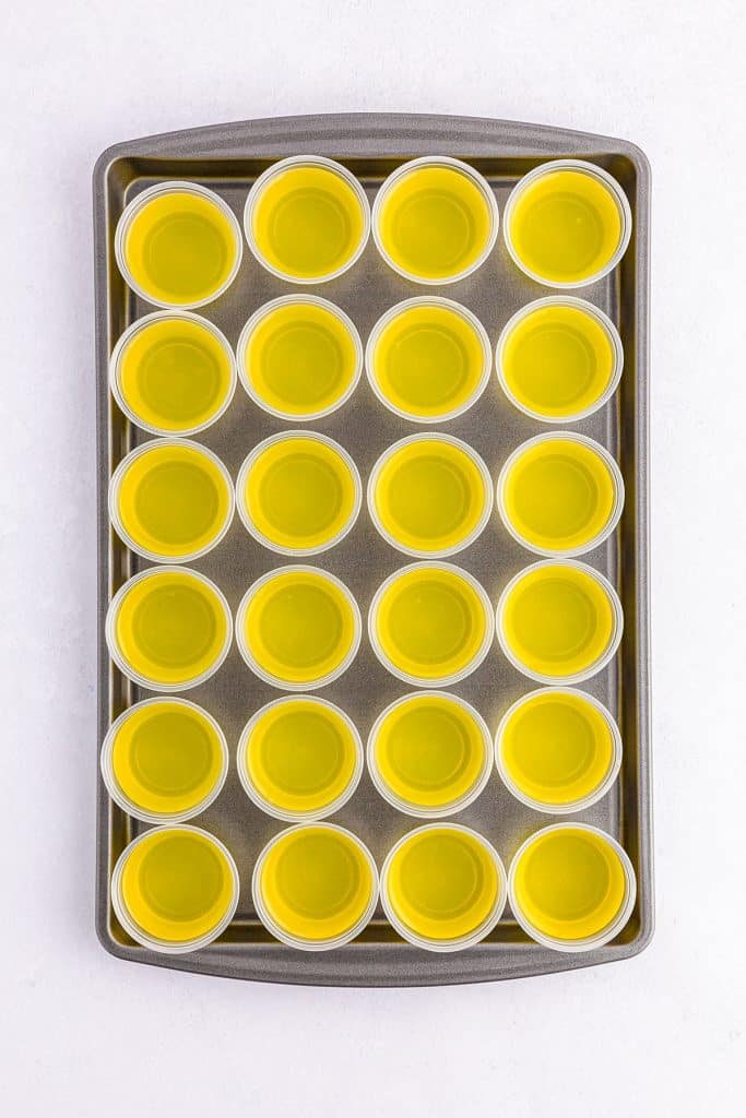 overhead shot of yellow jello shot cups on a baking sheet.