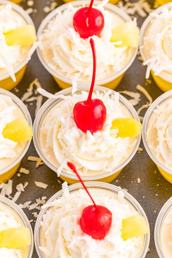 overhead pic of small jello shot cups topped with whipped cream, coconut, and cherries.