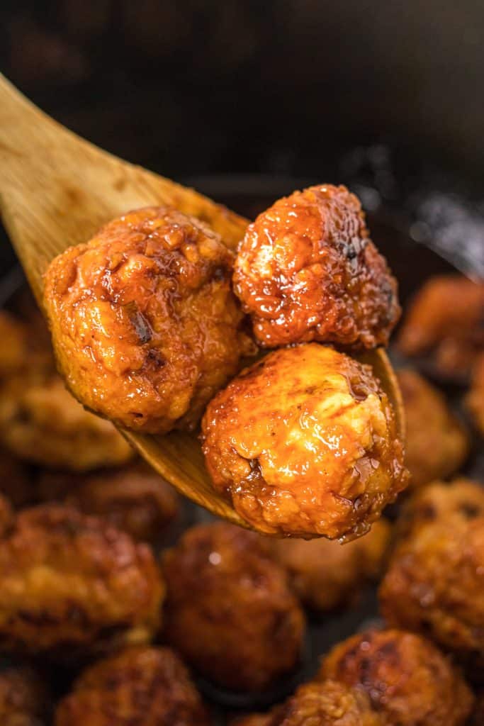 wood spoon lifting meatballs from a slow cooker.