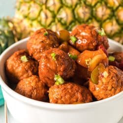 white bowl filled with hawaiian meatballs in front of a pineapple.
