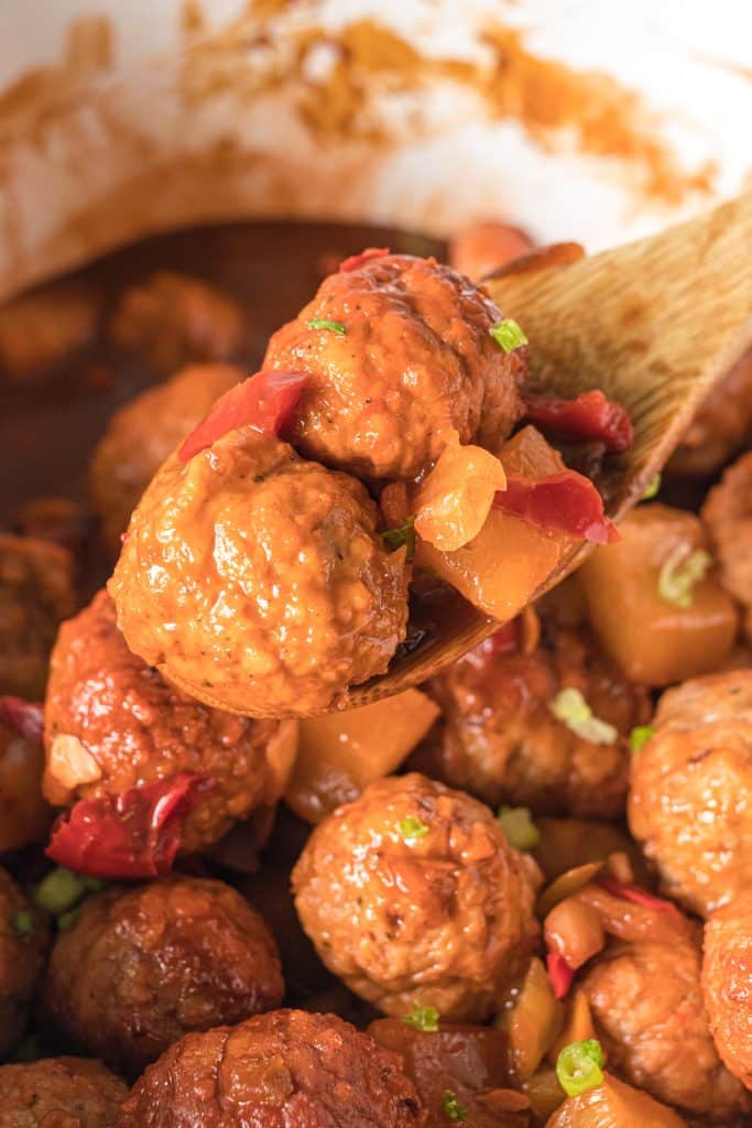 wooden spoon lifting hawaiian meatballs from a slow cooker.