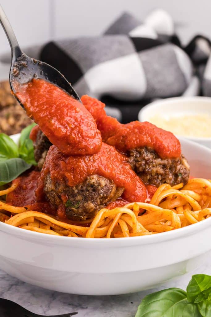 sauce being spooned over meatballs on pasta.