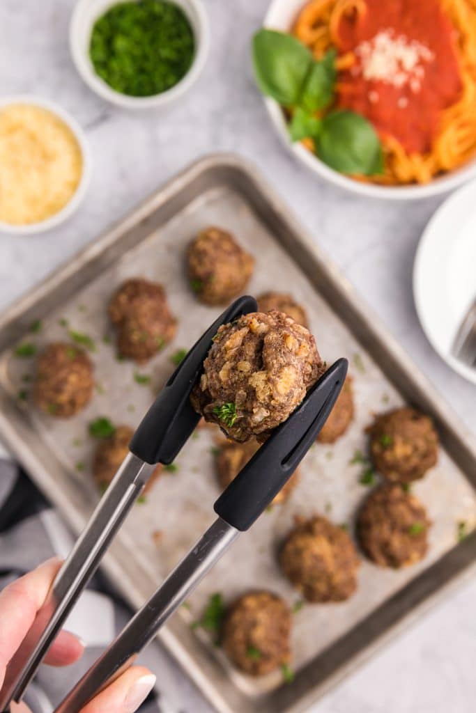 tongs holding a baked meatball.