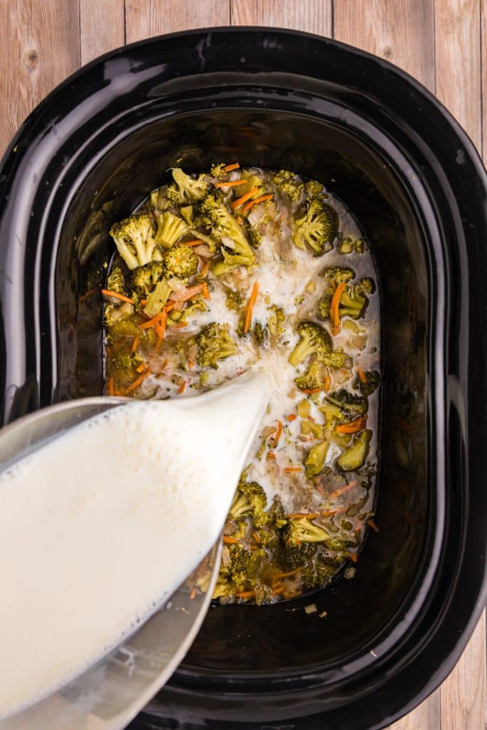milk pouring into crockpot broccoli cheese soup.