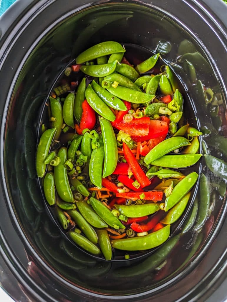 overhead shot of snap peas and red peppers in a crockpot.