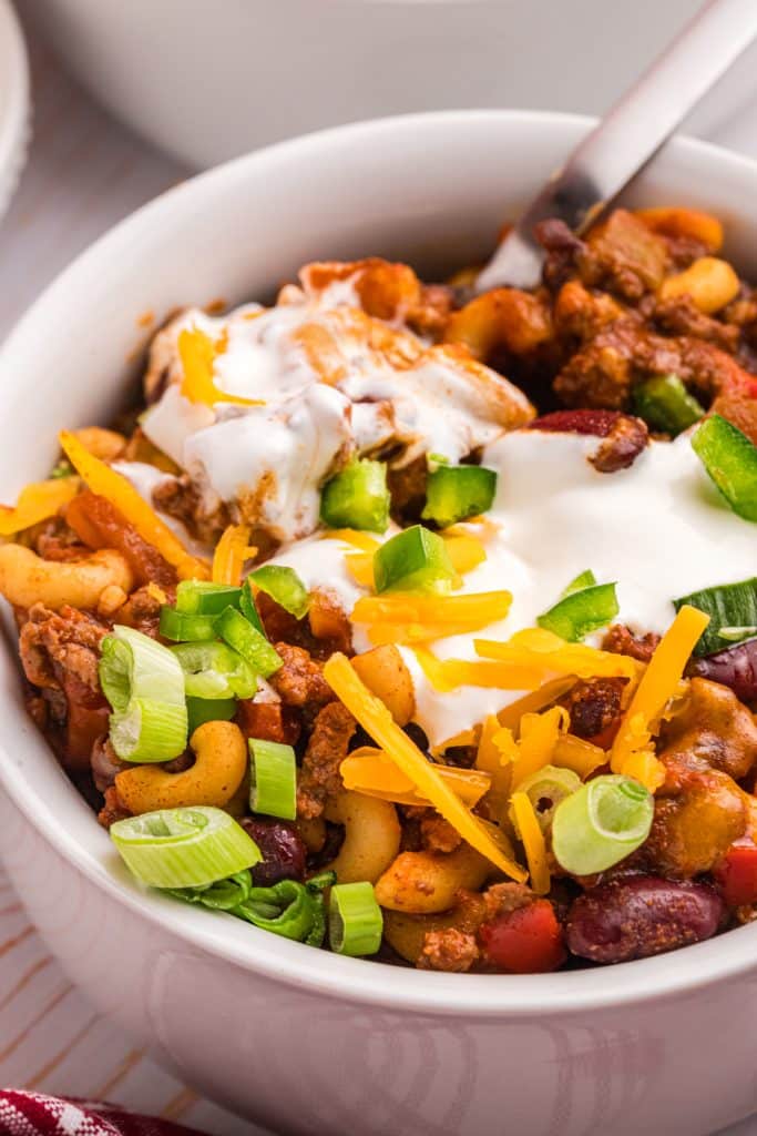 bowl of chili mac topped with sour cream, shredded cheese, and scallions.