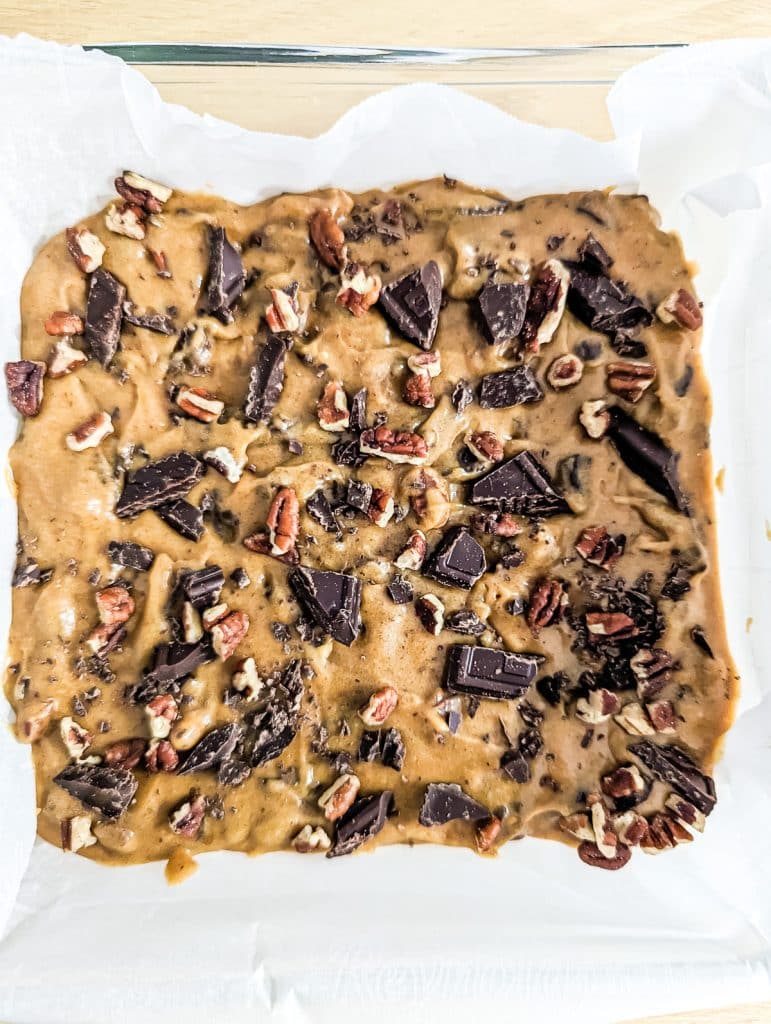 overhead shot of cookie dough in a baking dish topped with chocolate chunks and chopped pecans.