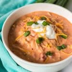 white bowl of buffalo chicken chili topped with sour cream, scallions, and shredded cheese.