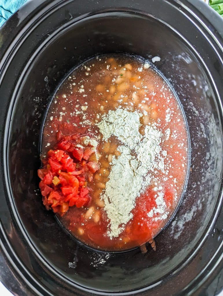 overhead shot of tomatoes, ranch seasoning, and beans in a crockpot.