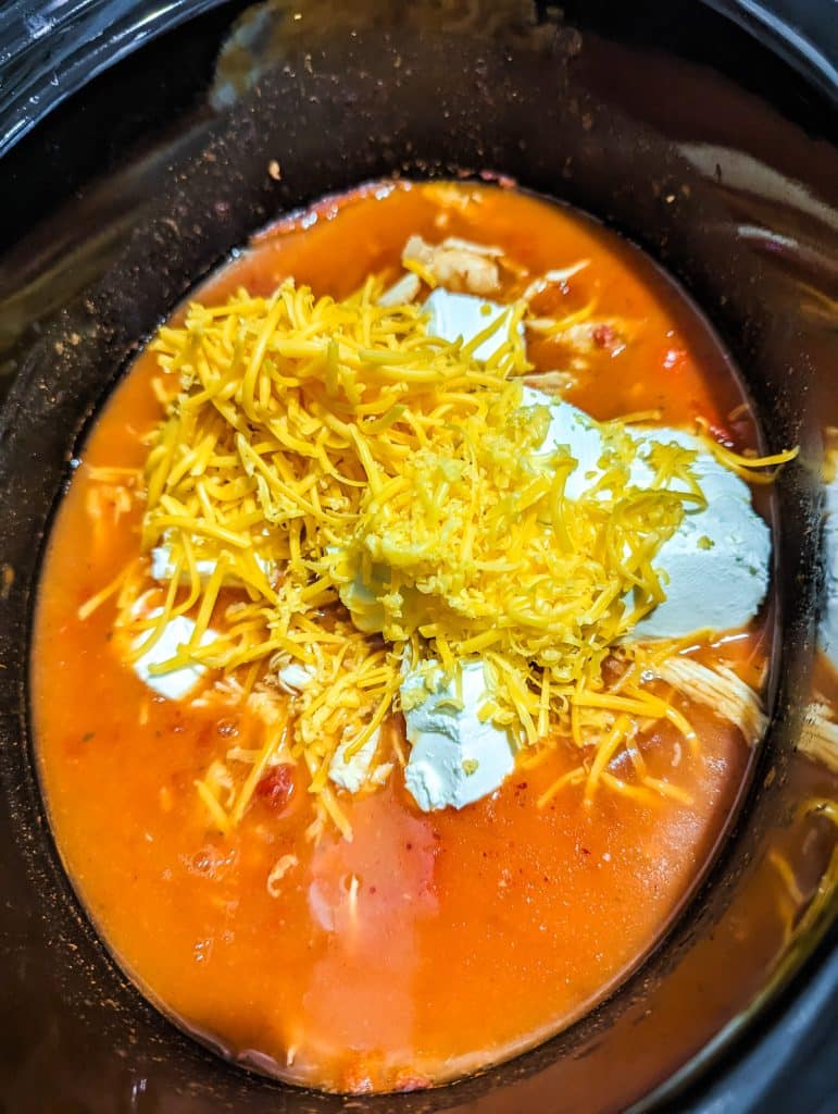 overhead shot of shredded cheddar and cubed cream cheese in a slow cooker.