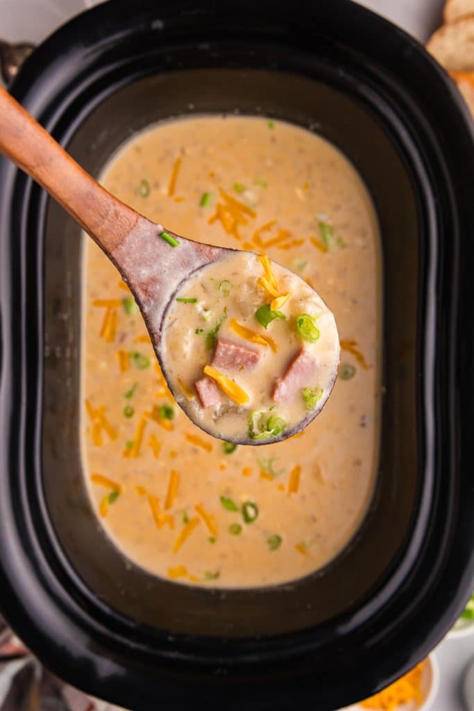 overhead shot of a ladle lifting ham & potato soup from a slow cooker.