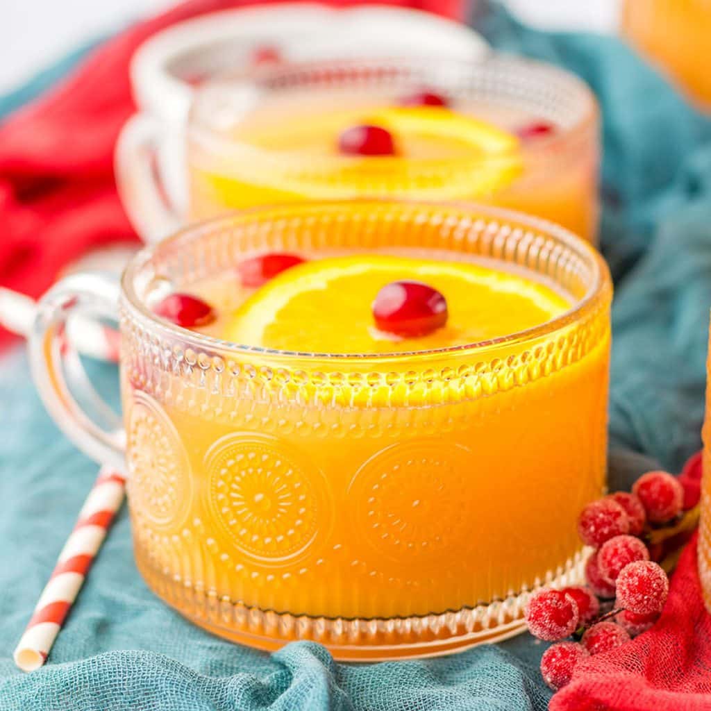 glass mug of christmas morning punch topped with cranberries & orange slices.