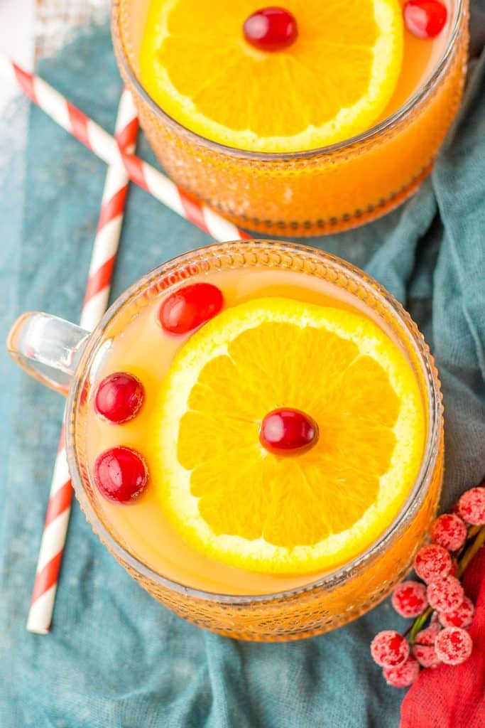 overhead shot of two mugs of christmas punch topped with orange slices and cranberries.