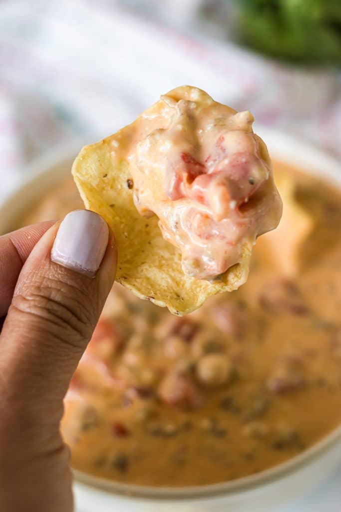 hand holding a tortilla chip dipped in sausage cheese dip.