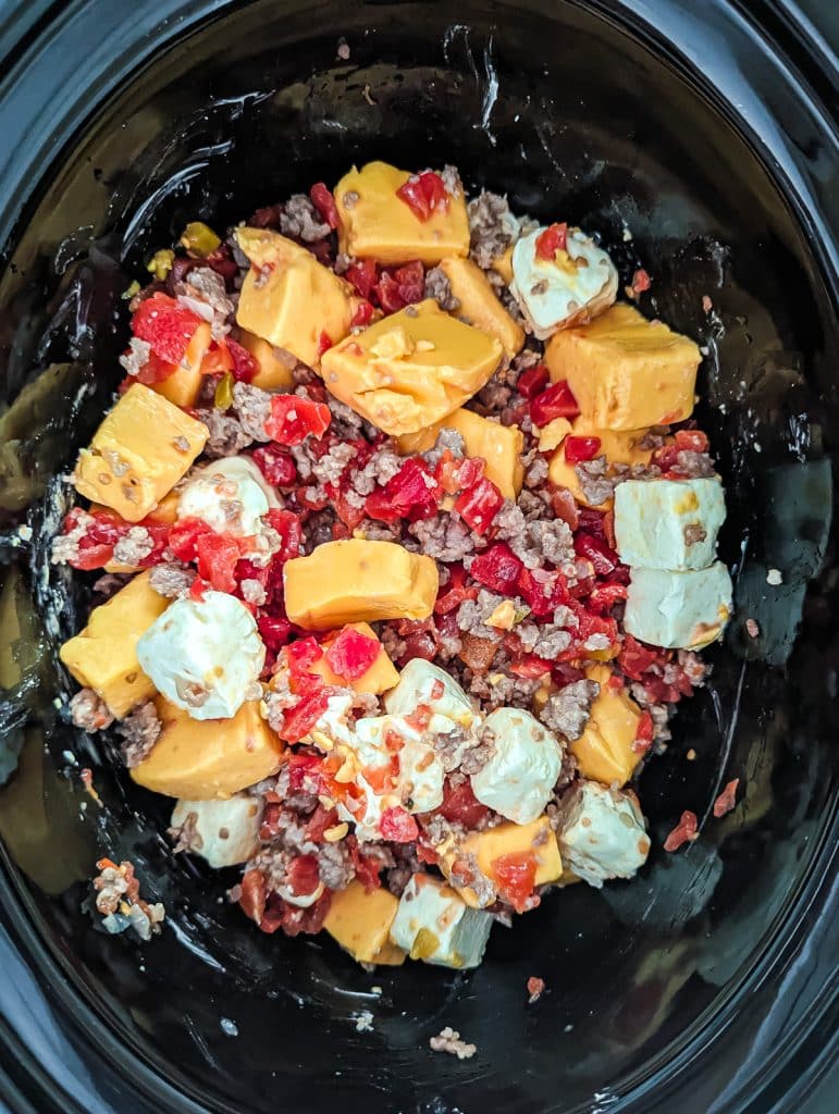 overhead shot of cream cheese, velveeta, rotel, and sausage mixed together in a crockpot.