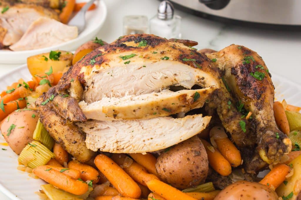 sliced whole chicken on a platter with carrots and potatoes.