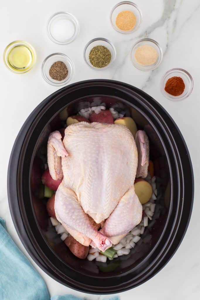 overhead shot of a raw whole chicken in a slow cooker.