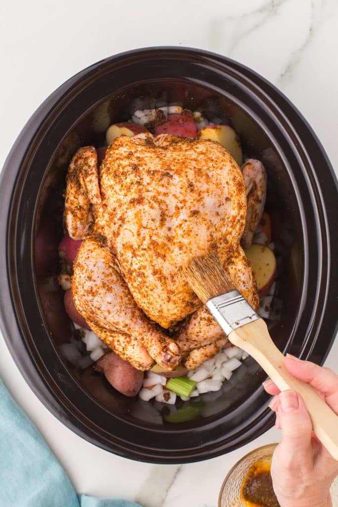 pastry brush brushing seasoning onto a whole chicken in a crockpot.