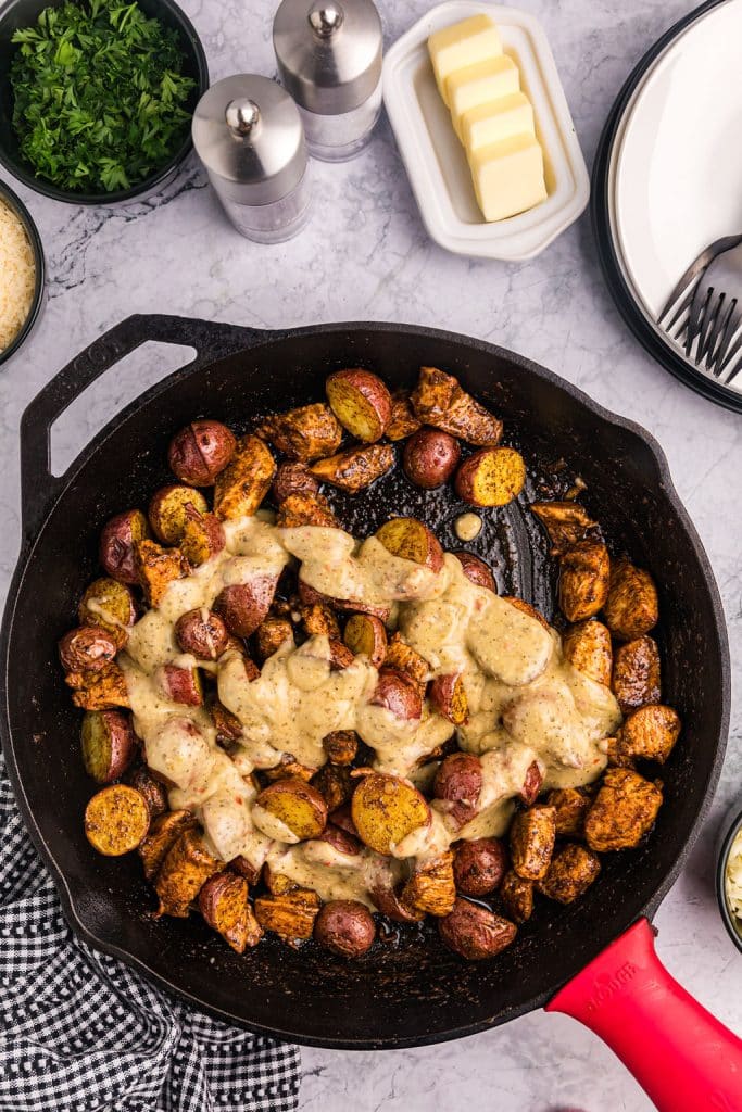 overhead shot of garlic parmesan sauce poured on chicken & potatoes in a skillet.
