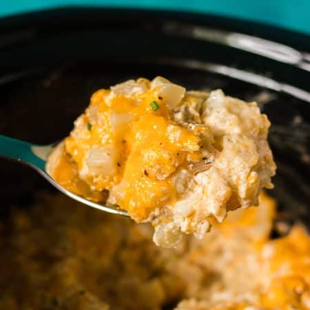 spoon lifting a scoop of cheesy potatoes from a slow cooker.