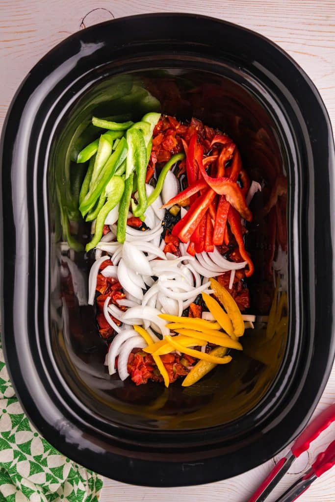 overhead shot of sliced bell peppers and onions in a black crockpot.