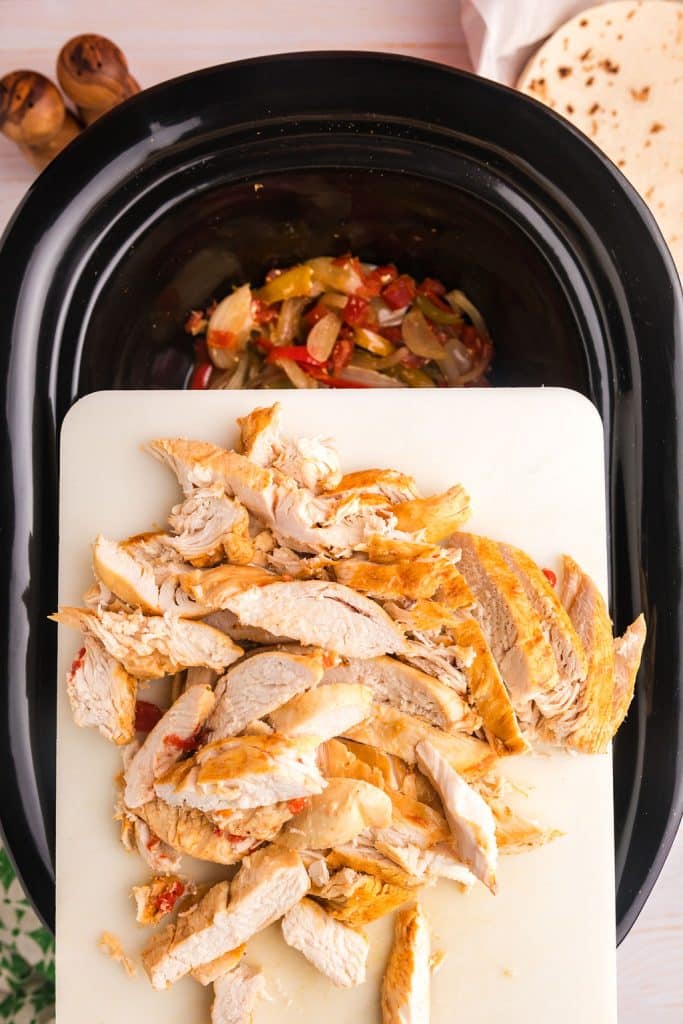 sliced chicken on a cutting board held over a slow cooker.