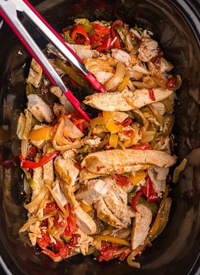 tongs in a slow cooker with chicken fajitas.