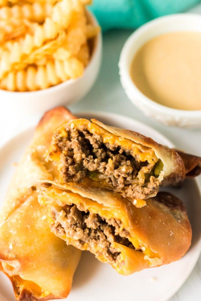 cheeseburger egg roll cut in half with a side of french fries.