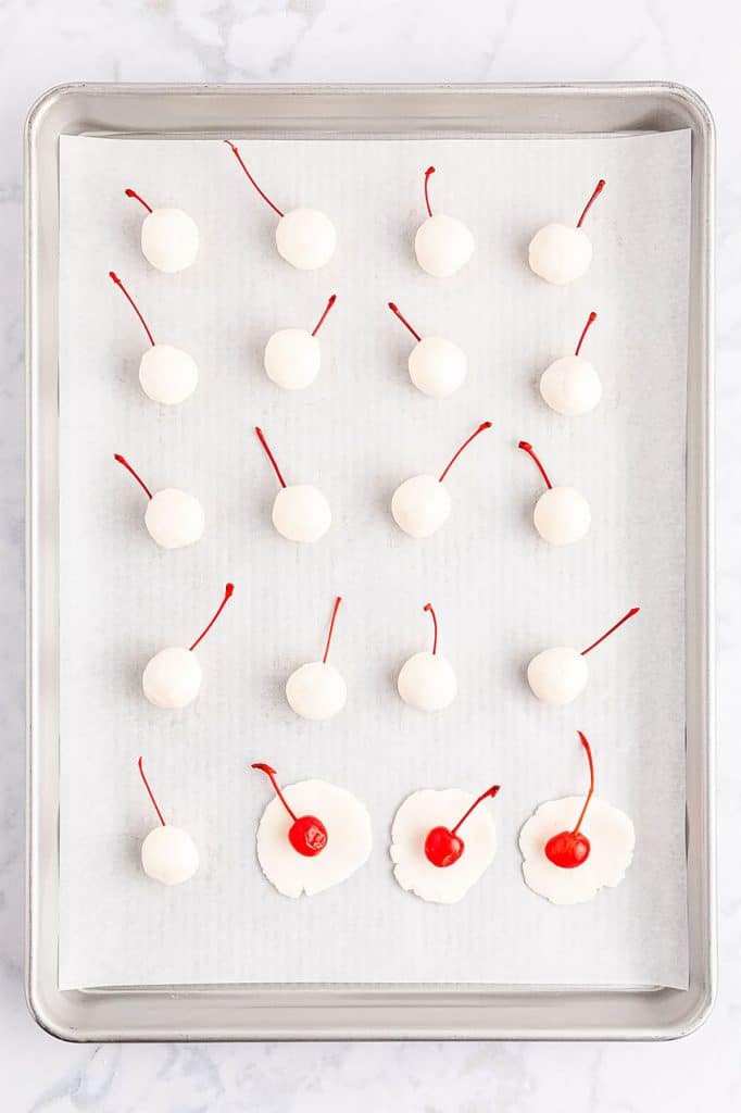 overhead shot of cherries being covered in sugar dough on a baking sheet.