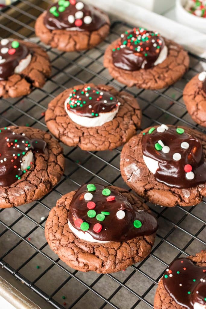 hot chocolate cookies with chocolate frosting & christmas sprinkles on a cooling rack.