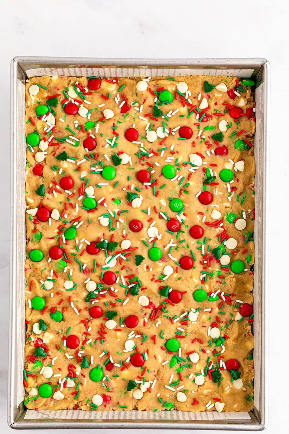 overhead shot of cookie dough in a baking dish topped with red & green sprinkles.