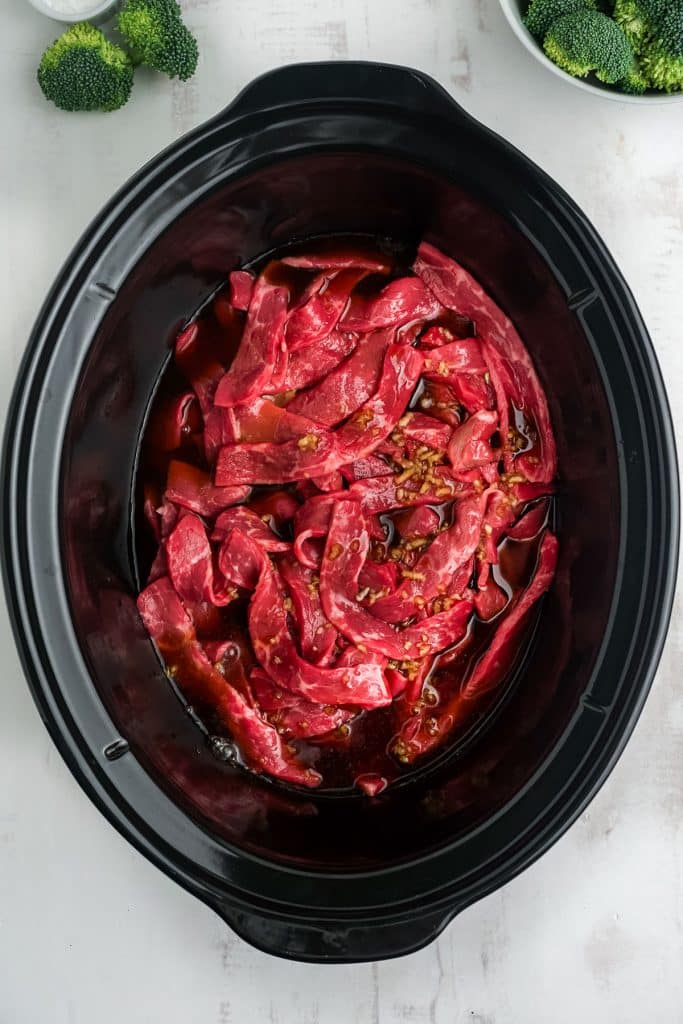 overhead shot of raw beef cut into strips in a slow cooker.