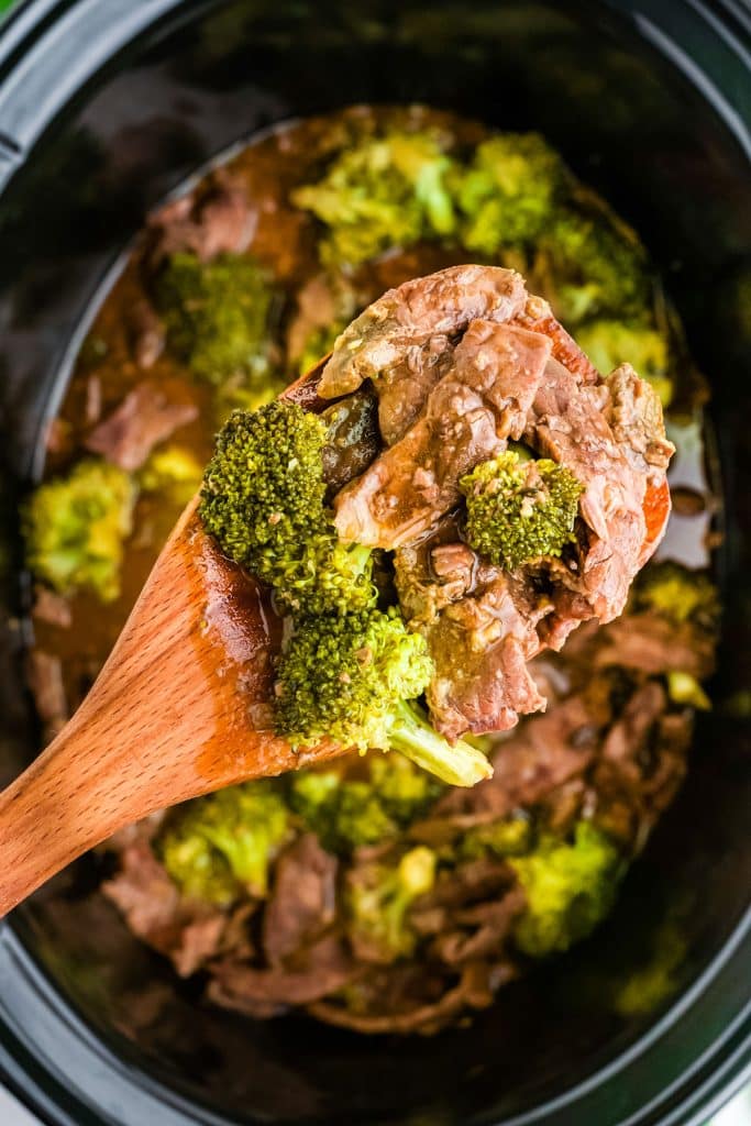 wood spoon lifting beef and broccoli from a slow cooker.