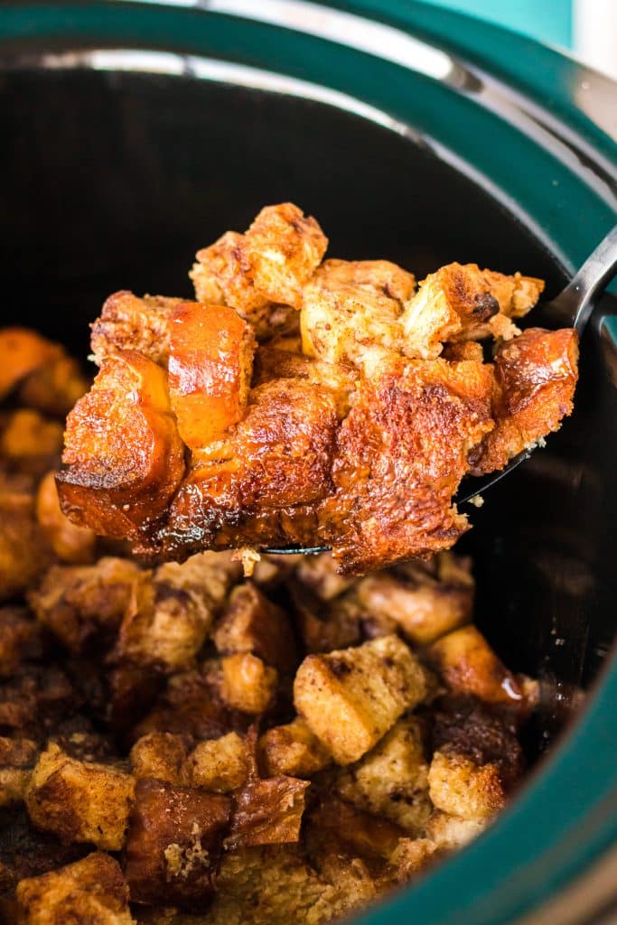 spoon lifting a scoop of french toast casserole from a slow cooker.
