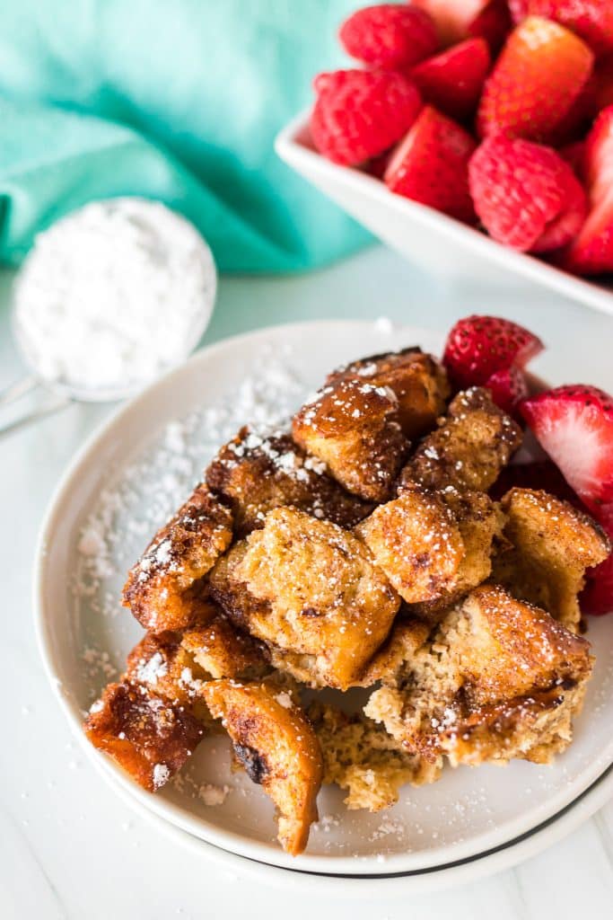 plate of french toast casserole topped with powdered sugar next to a bowl of berries.