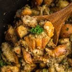 wooden spoon scooping stuffing from a slow cooker.