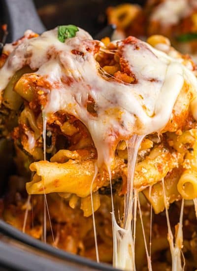 spoon lifting cheesy ziti from a slow cooker.