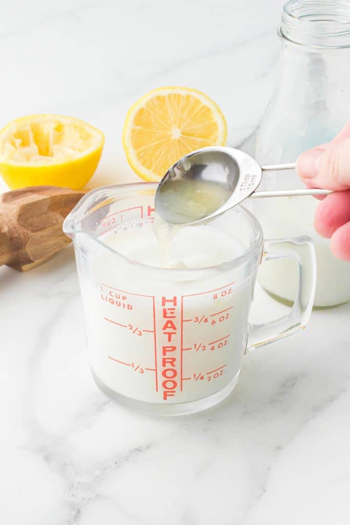 spoon pouring lemon juice into a cup of milk.