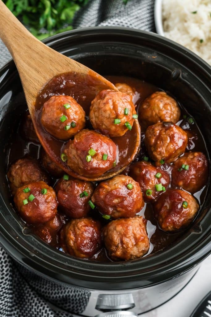 wooden spoon lifting meatballs from a slow cooker.