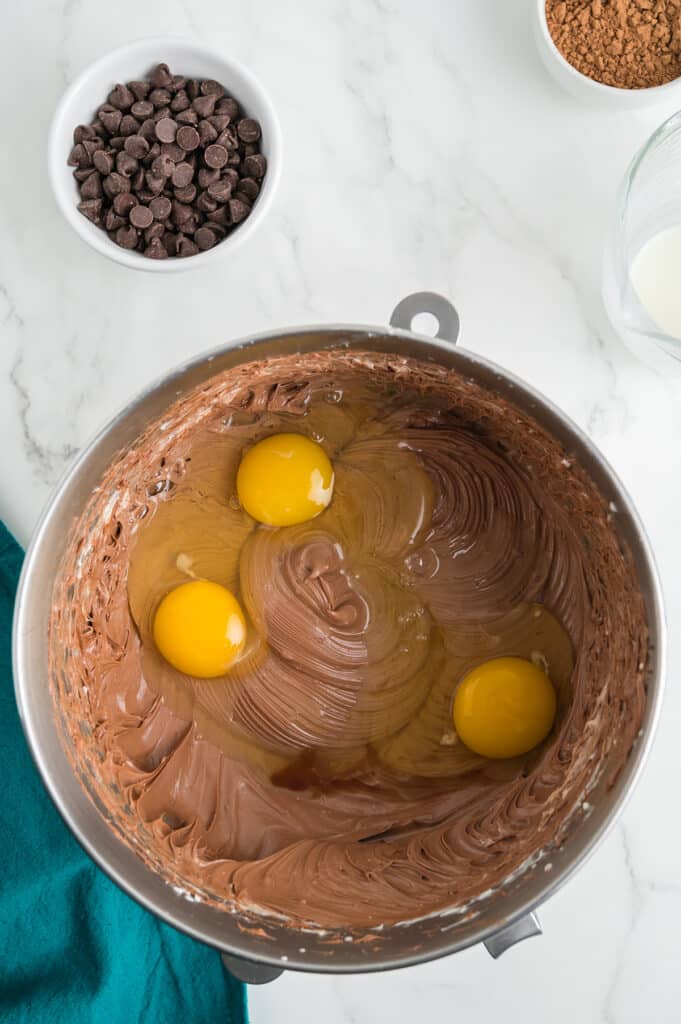three eggs cracked into a chocolate cheesecake batter.