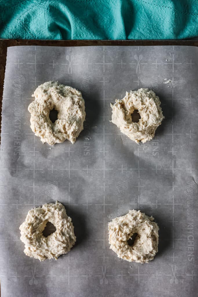 overhead shot of 4 raw bagels on a baking sheet.