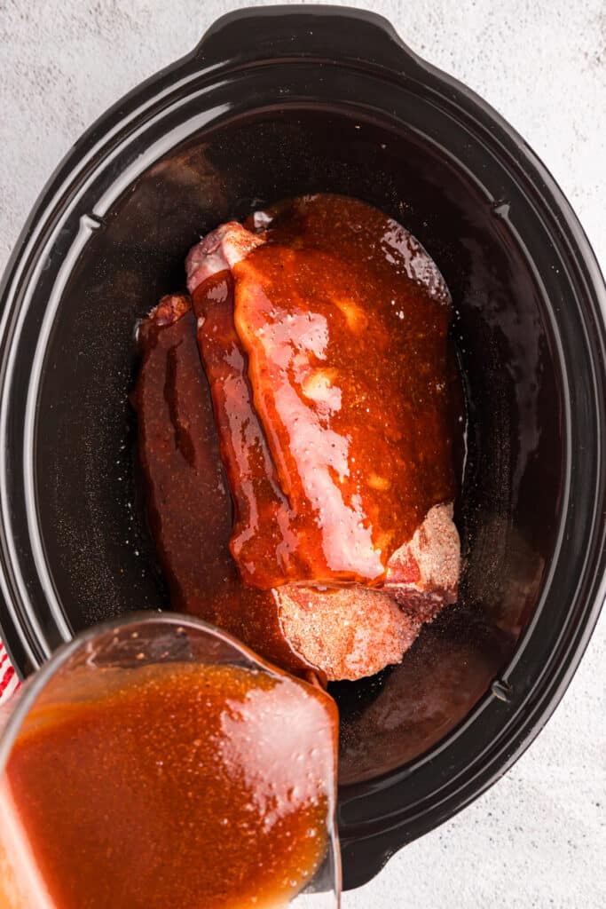 sauce pouring over ribs in a crockpot.