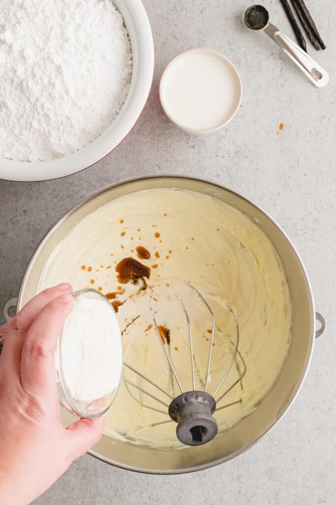 hand pouring vanilla into buttercream in a mixing bowl.