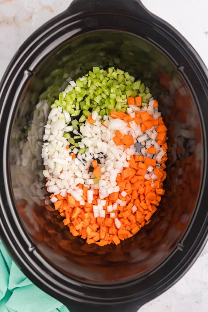 overhead shot of diced carrots, onion, and celery in a slow cooker.