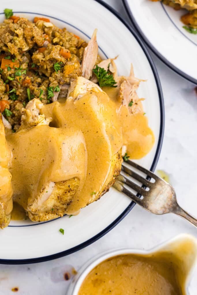 fork poking into roasted chicken with gravy and stuffing.