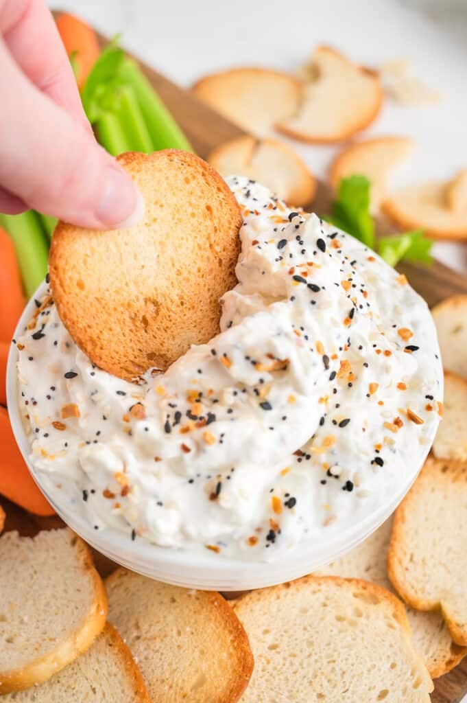 hand dipping a bagel chip into creamy bagel dip.
