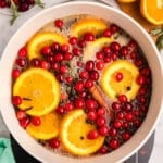 A pot with orange slices, cranberries, rosemary, and cinnamon sticks in liquid.