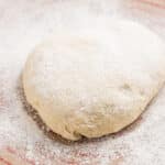 A round ball of dough dusted with flour on floured surface.