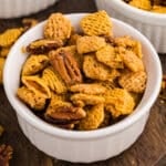 Bowl of butter pecan snack mix on a wooden board.