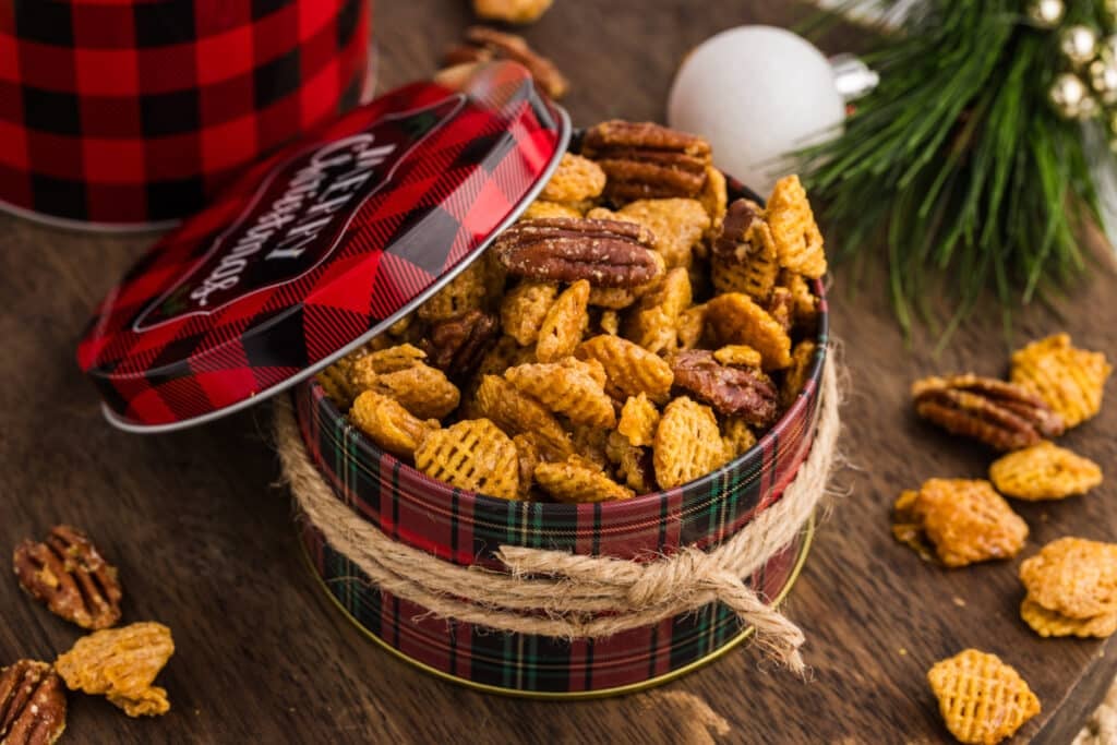 Butter pecan snack mix in a red plaid holiday tin with twine around it.